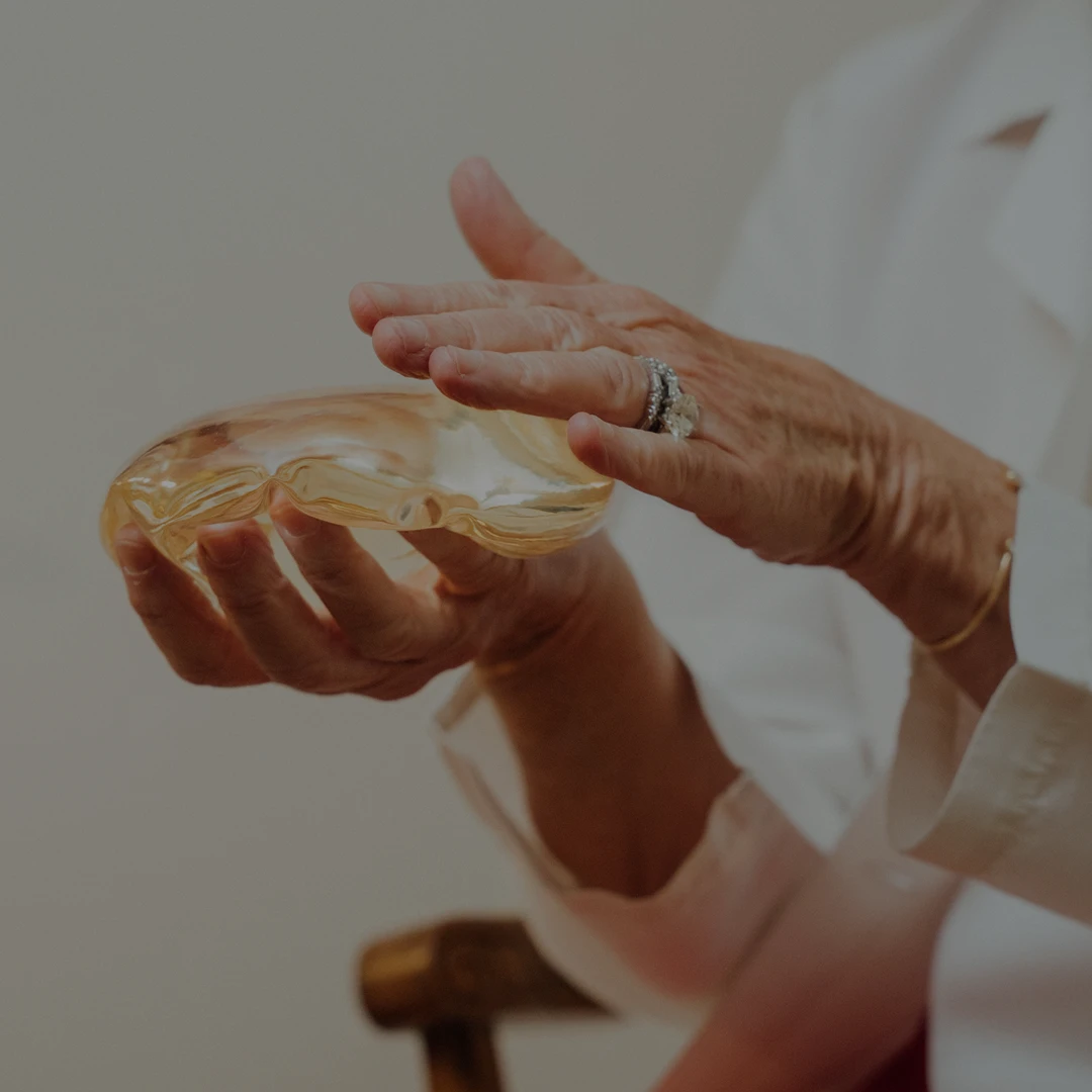 A close-up shot of a surgeon's hands carefully demonstrating the texture and flexibility of a clear breast implant.