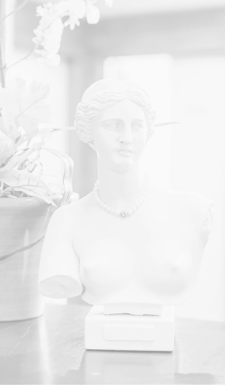A grayscale, faded image of a classical Roman-style female bust wearing a pearl necklace, positioned next to an orchid plant.