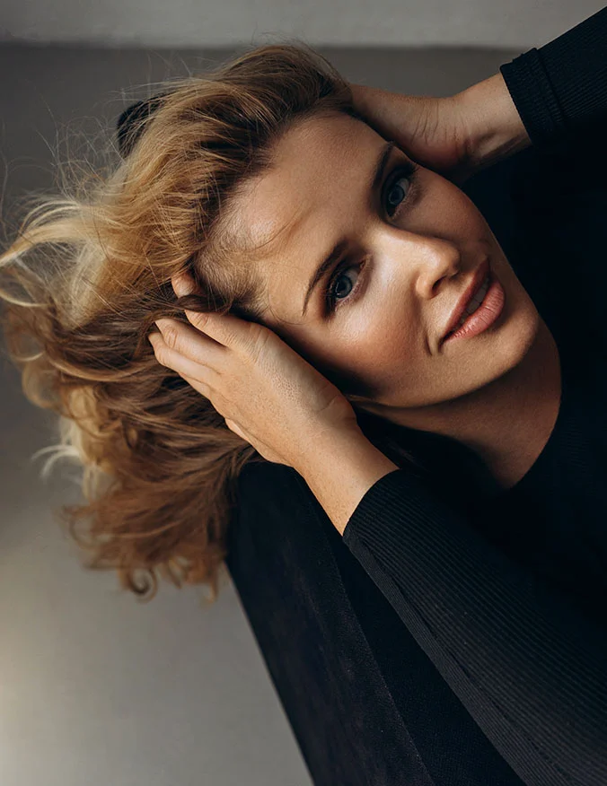An artistic, high-angle shot of a woman with blonde hair, looking upward with a bright, open expression that highlights a smooth forehead and lifted brow area.