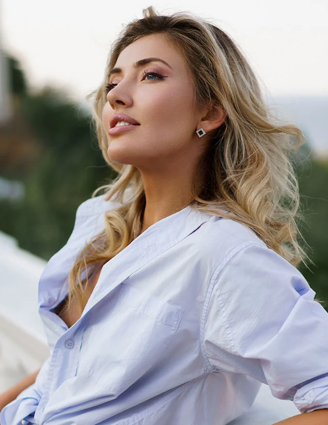 A profile shot of a blonde woman in a light blue button-down shirt looking toward the sky, highlighting a sharp and defined jawline.