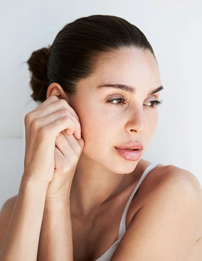 A portrait of a woman with her hair in a bun looking to the side, highlighting natural-looking facial volume and smooth skin.