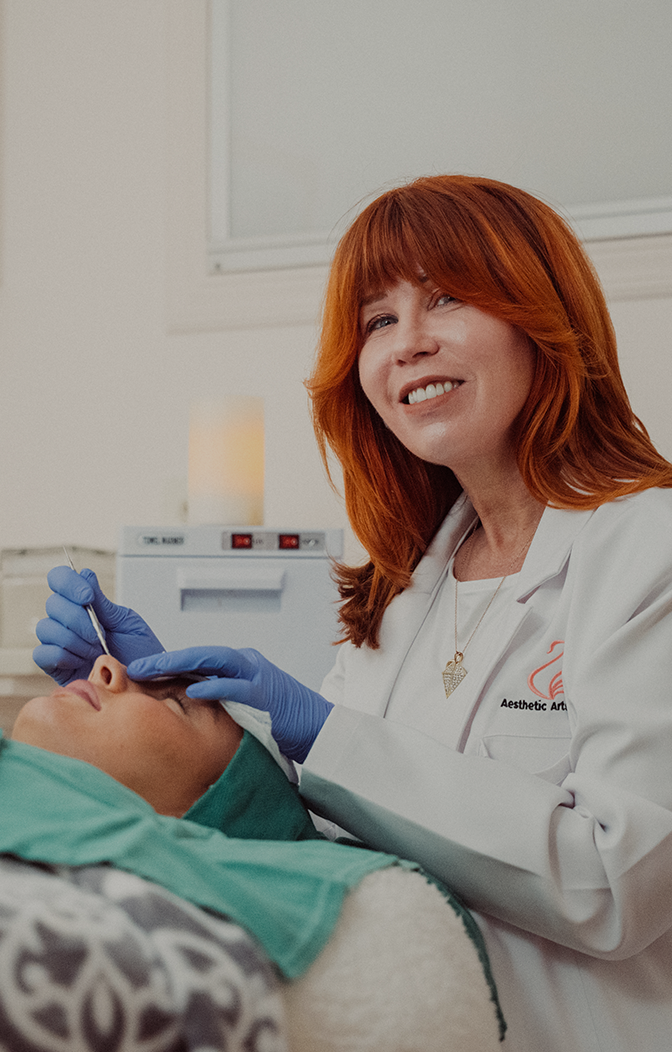 A close-up of a medical professional with vibrant red hair and a white coat performing a precise skin treatment on a patient’s face in a clinical setting.