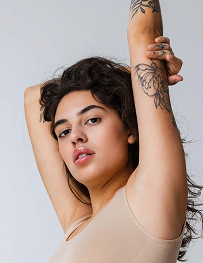 A woman with her arms raised, showcasing floral tattoos that are being targeted for laser removal treatments.